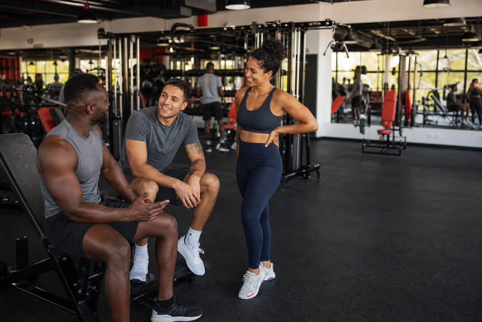 Three Caribbean training partners talking between sets in a commercial gym